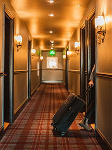 Persoon met koffer die een kamer binnenloopt in de gang van een hostel.