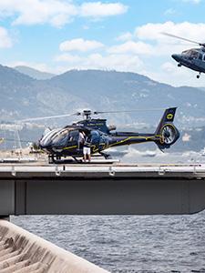 Helikopter op een landingsplatform met kust en bergen op de achtergrond.