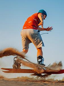 Persoon sandboardt van een duin tijdens een georganiseerde en adrenalinevolle activiteit.